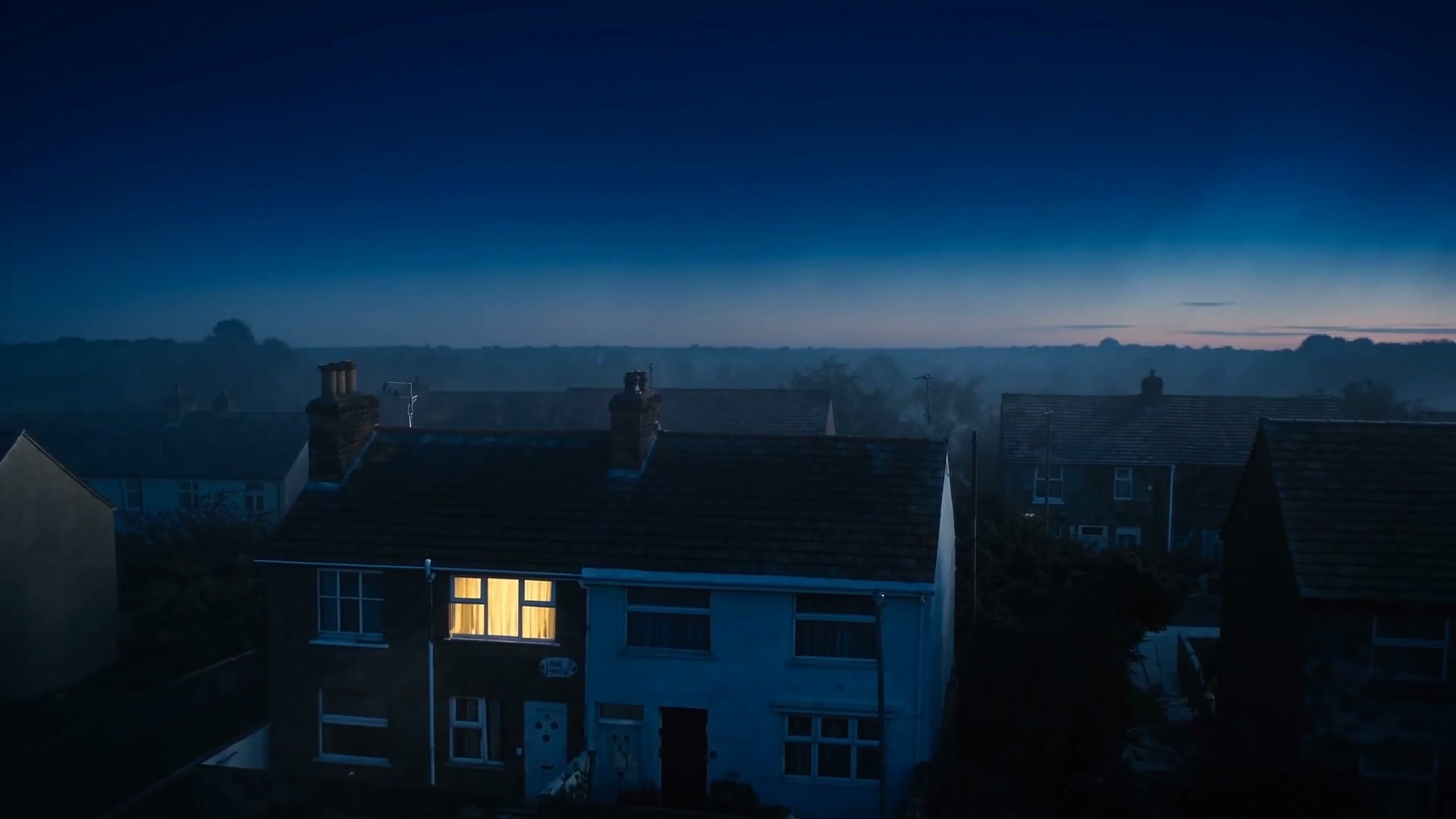 The film's resting frame: a terraced house at dawn with one warm window glowing.